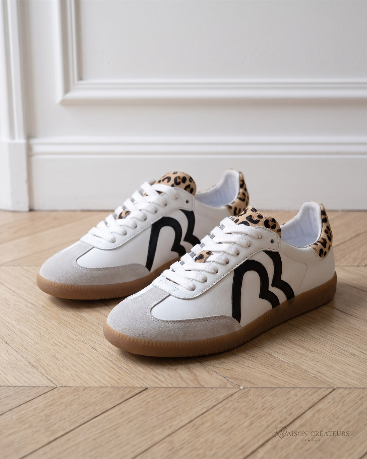Baskets Billie blanches à empiècements léopard et motif noir, posées sur un parquet en chevrons