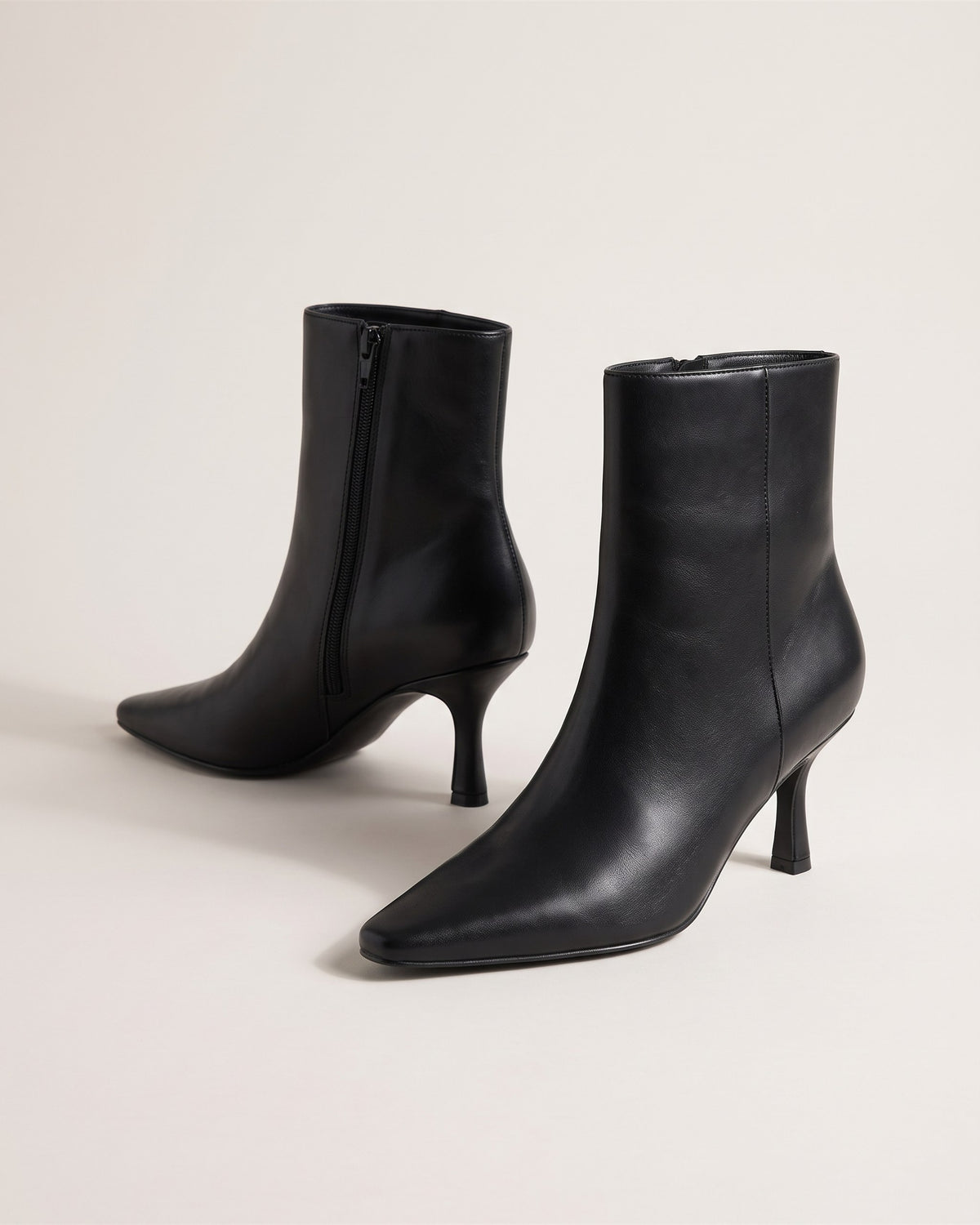 Bottines noires élégantes à talon fin et bout pointu, vue de face sur fond pierre