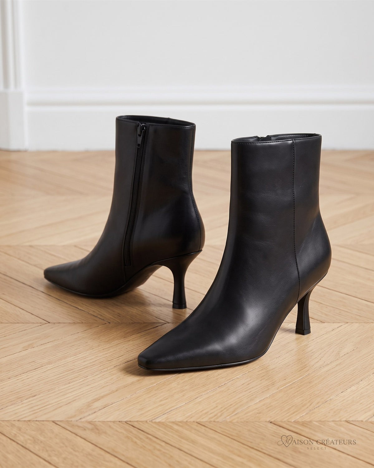 Bottines noires élégantes à talon fin et bout pointu, posées sur un parquet en chevrons