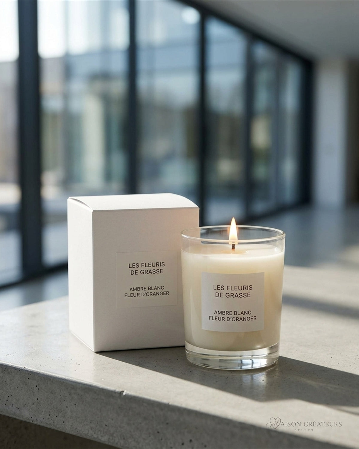 Bougie parfumée 130 g Ambre Blanc Fleur d Oranger, verre et coffret, posé sur du béton dans un atrium lumineux