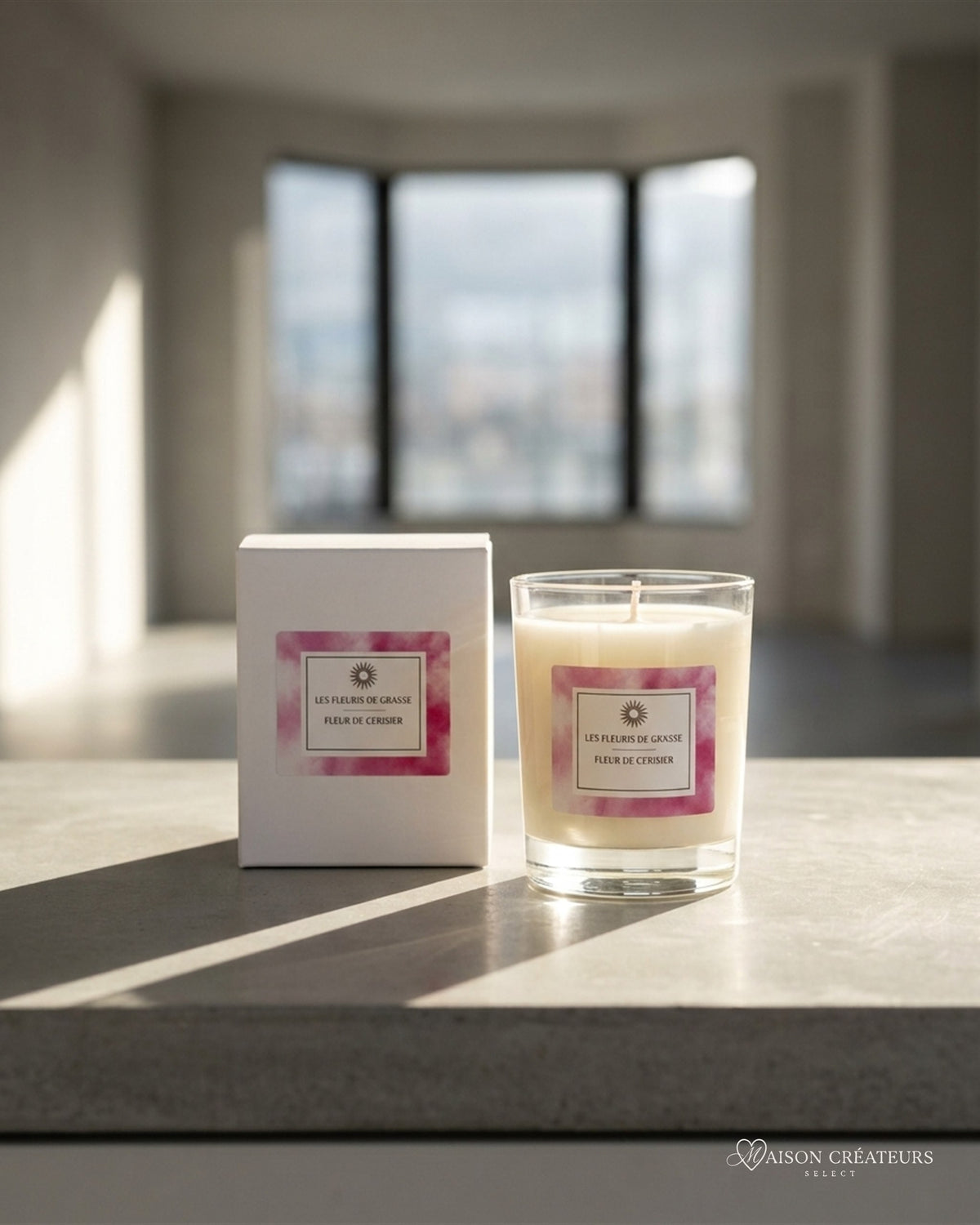 Bougie parfumée 130 g Cerisiers en fleurs, verre et coffret rose, posé sur du béton dans un atrium lumineux