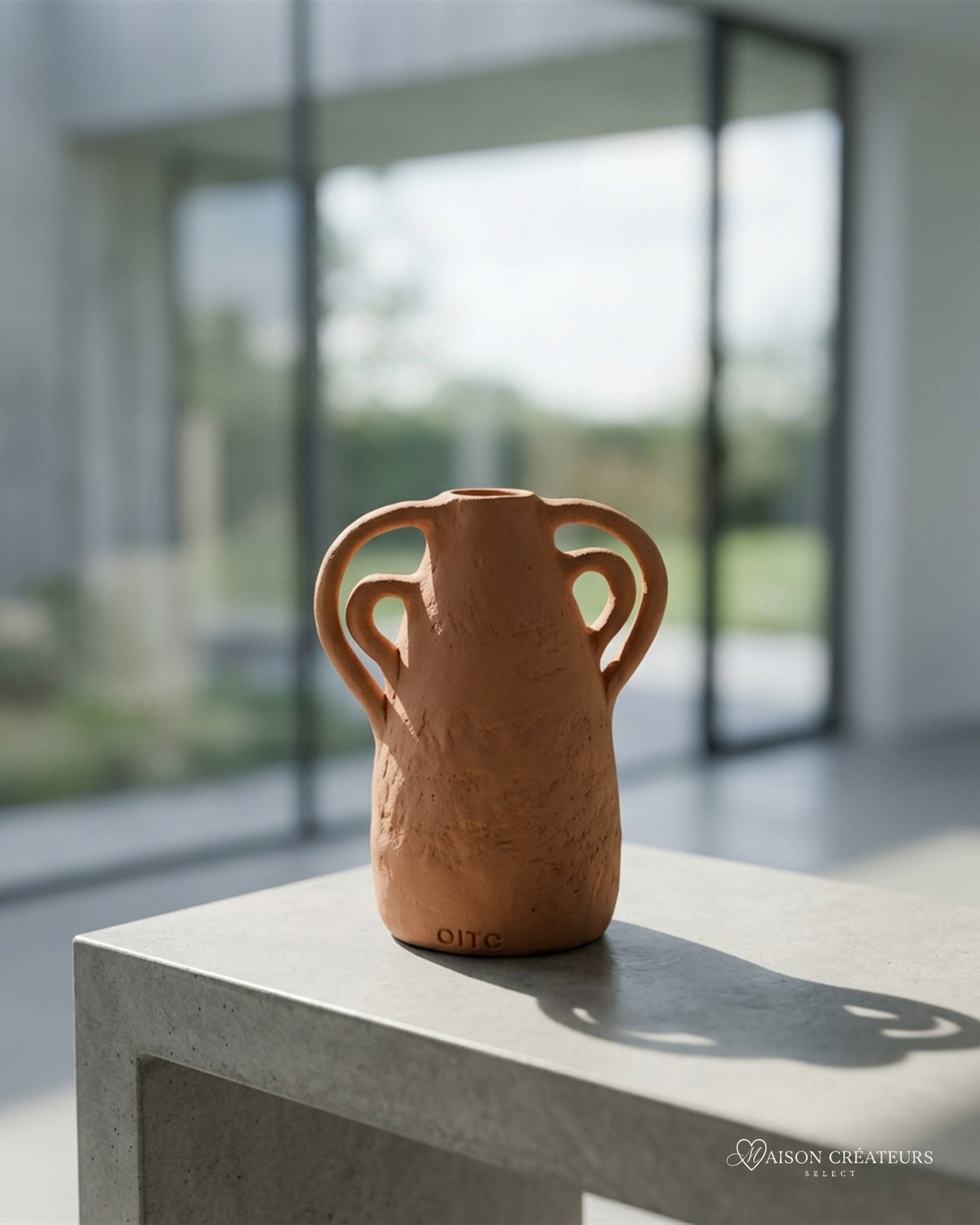 Vase amphore artisanal en céramique terracotta fait main au Portugal, posé sur du béton dans un atrium lumineux