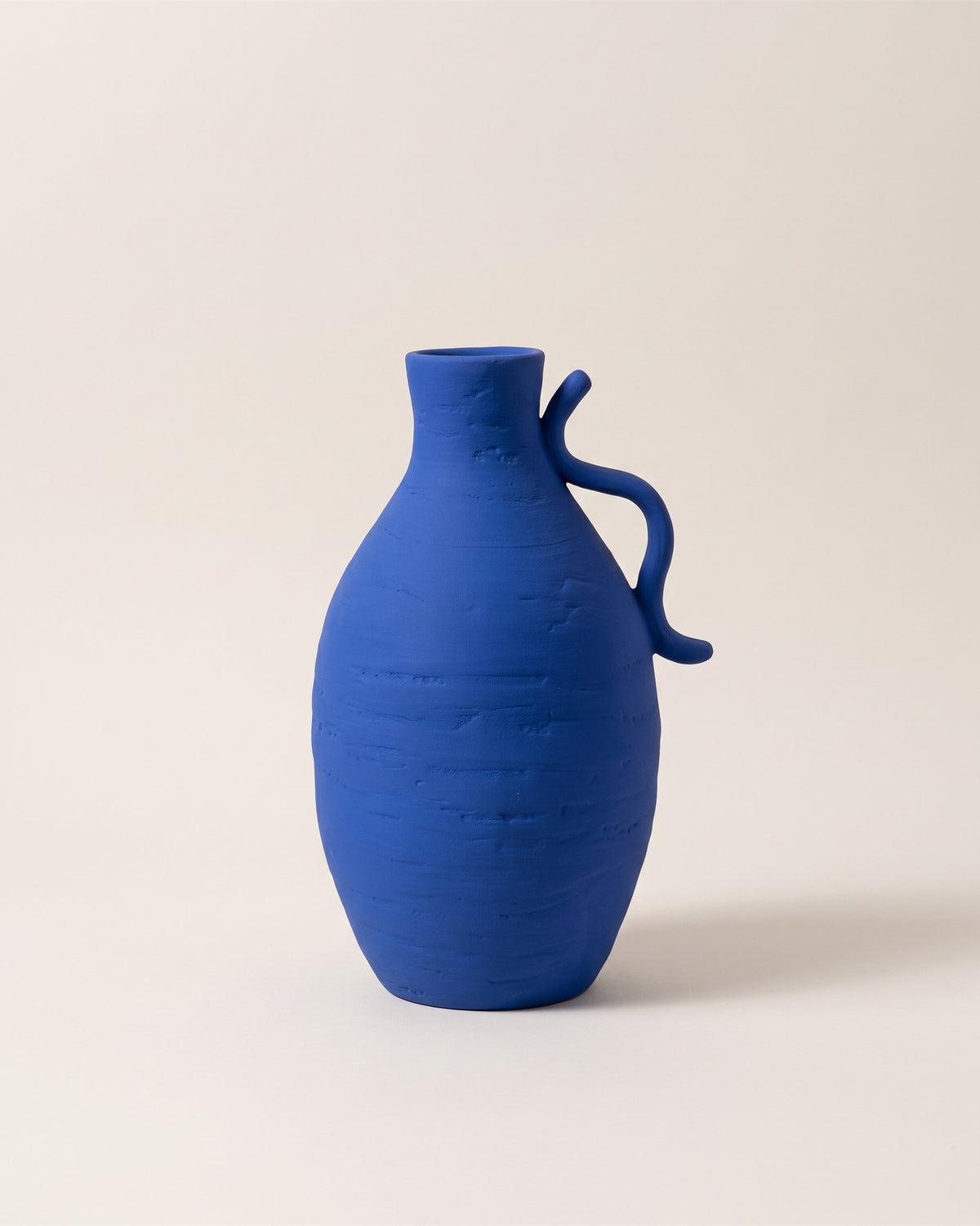 Vase Creta en céramique bleu Klein à anse, vue de face sur fond pierre