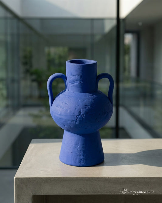 Amphore artisanale en céramique bleu Klein à deux anses, posé sur du béton dans un atrium lumineux