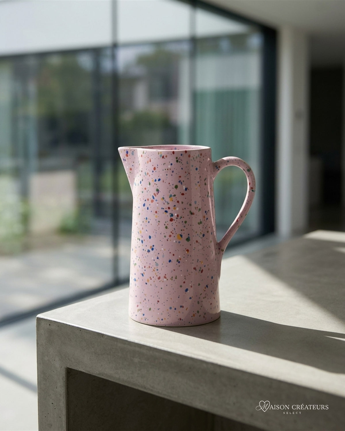 Pichet de fête lilas moucheté 1,5 L en céramique, posé sur du béton dans un atrium lumineux