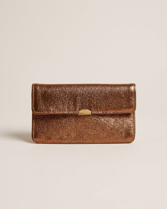 Le porte-monnaie compact tout-en-un en cuir métallisé noisette, forme enveloppe à rabat et fermoir doré, vue de face sur fond pierre
