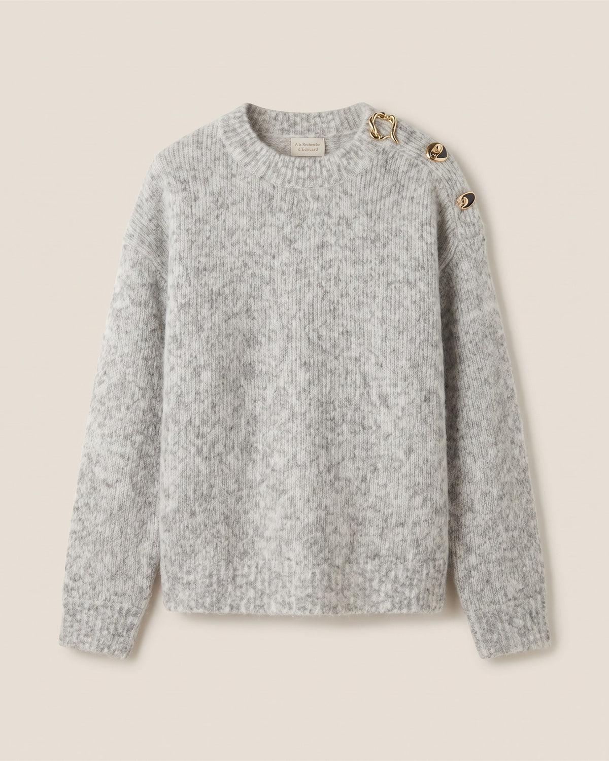 Pull en maille chinée gris clair à boutons bijoux sur l épaule, vue de face sur fond pierre