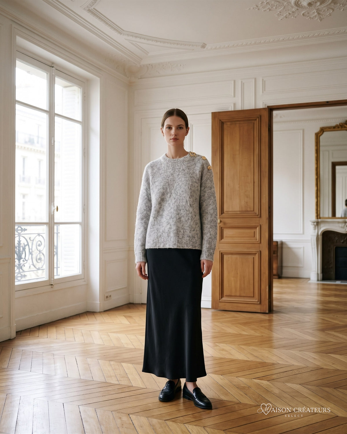 Pull en maille chinée gris clair à boutons bijoux sur l épaule, porté dans un salon haussmannien