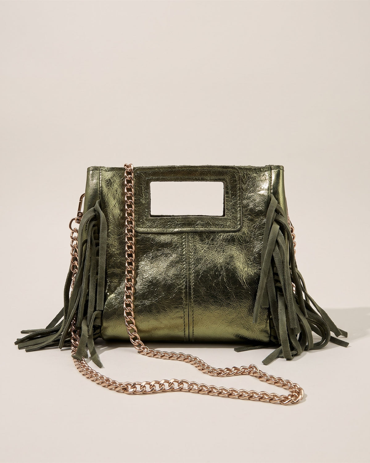 Le sac Marion Small en cuir irisé vert métallisé, forme carrée à poignée découpée, franges sur les côtés et chaîne dorée, vue de face sur fond pierre