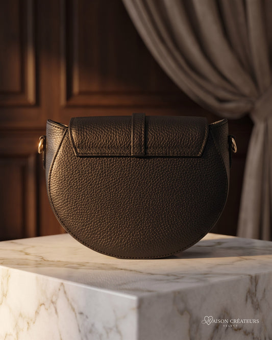Le sac bandoulière Madelena en cuir grainé noir posé sur un bloc de marbre blanc en boutique
