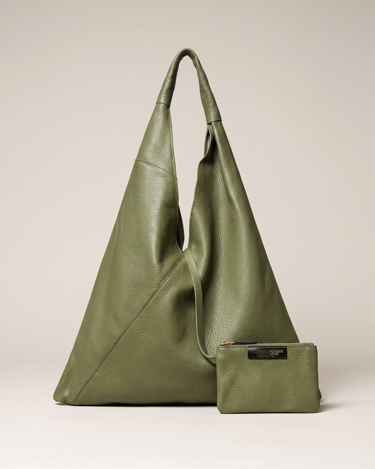Le sac Nomade en cuir grainé kaki, forme triangulaire souple portée épaule, avec sa petite pochette assortie, vue de face sur fond pierre