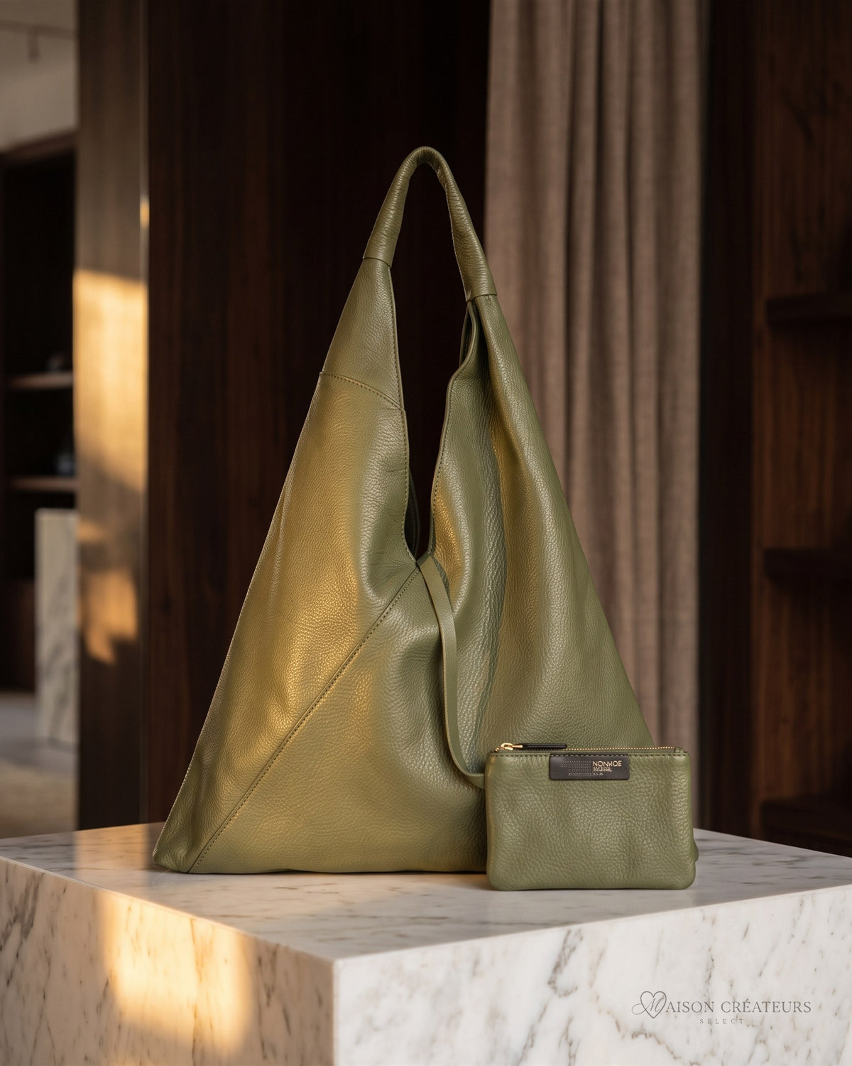 Le sac Nomade en cuir grainé kaki posé sur un bloc de marbre blanc en boutique