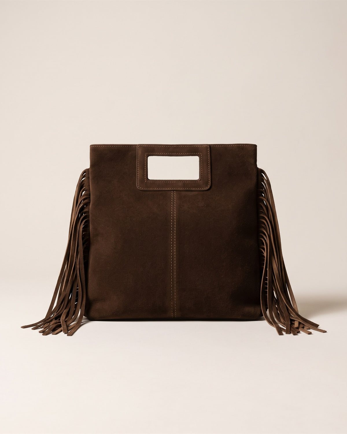 Le sac Solène en cuir suède italien chocolat, forme rectangulaire haute à poignée découpée et franges sur les côtés, vue de face sur fond pierre
