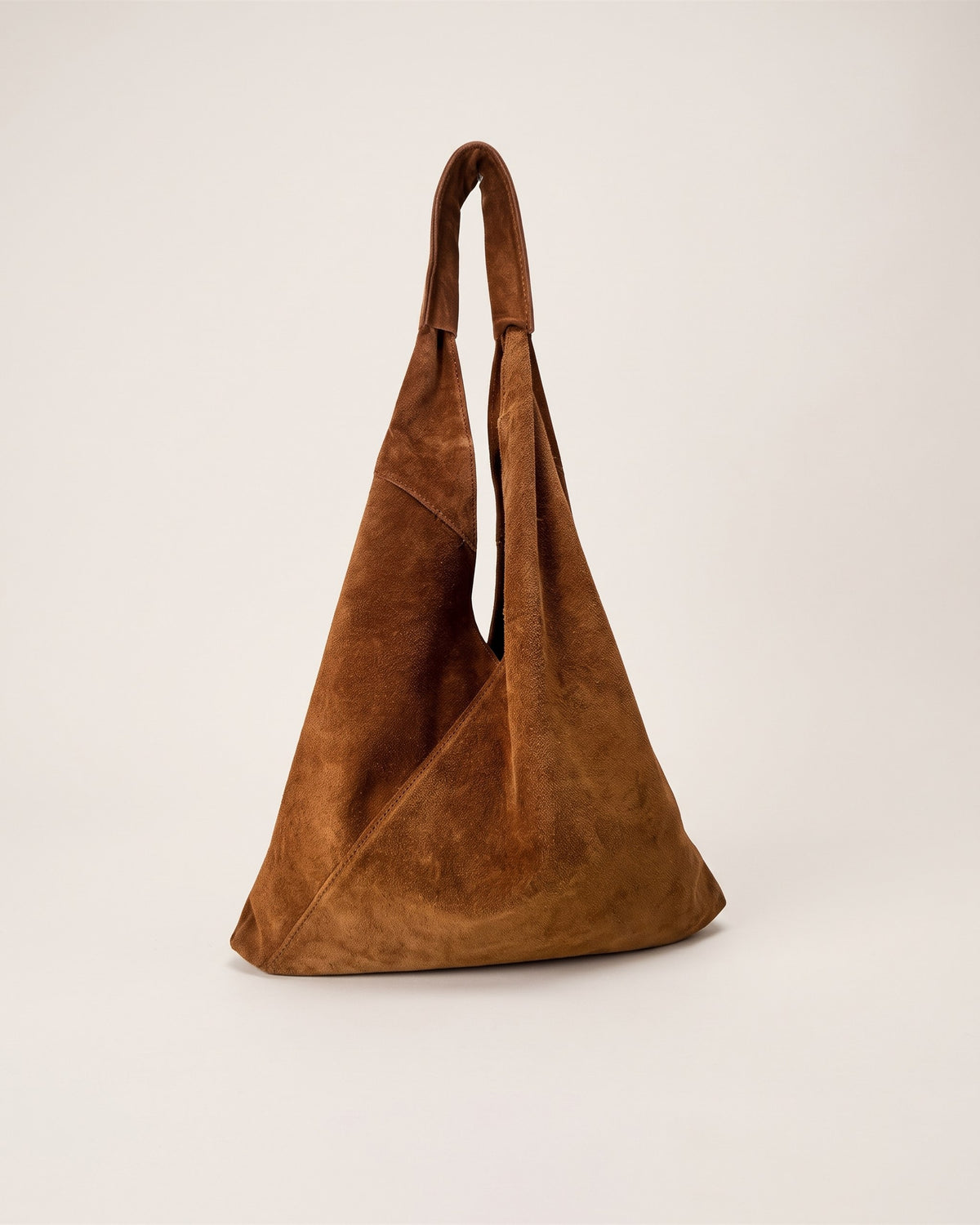 Le sac Nomade en cuir suède camel, forme triangulaire souple portée épaule, vue de face sur fond pierre