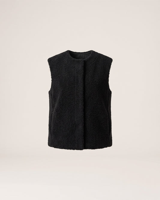 Veste sans manches noire en moumoute, vue de face sur fond pierre